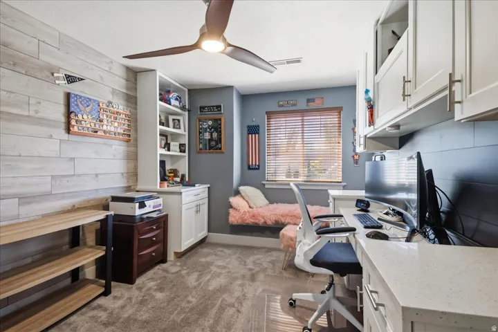 Built-in desk with a light-colored countertop, white upper and lower cabinetry, and a ceiling fan