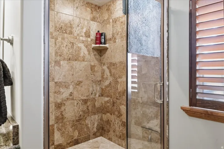 Tiled shower enclosure with a glass door, built-in corner shelf, and neutral-toned wall tiles featuring a decorative tile band