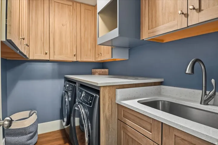 Laundry area featuring wood cabinetry, stone-finish countertops, and a stainless steel sink with a gooseneck faucet