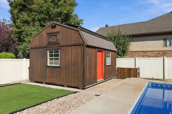 Wood-sided shed with a metal roof, white vinyl fencing, and a concrete pool deck