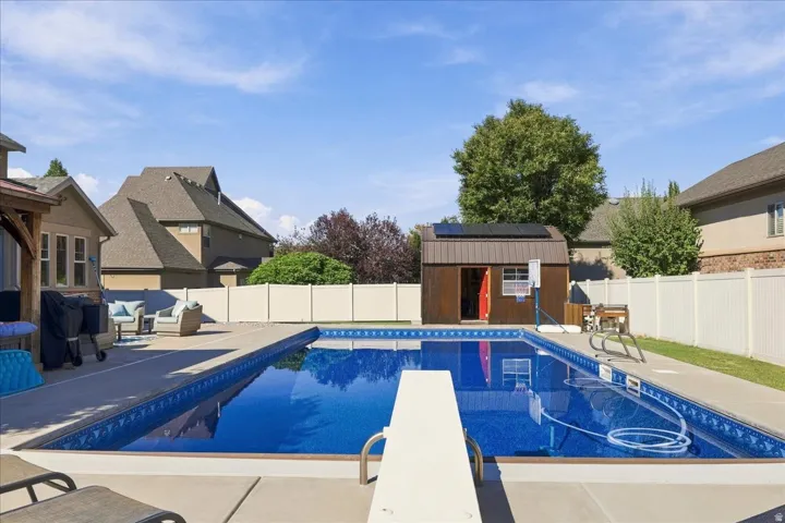 In-ground swimming pool with a diving board, surrounding concrete patio, and a dedicated storage shed
