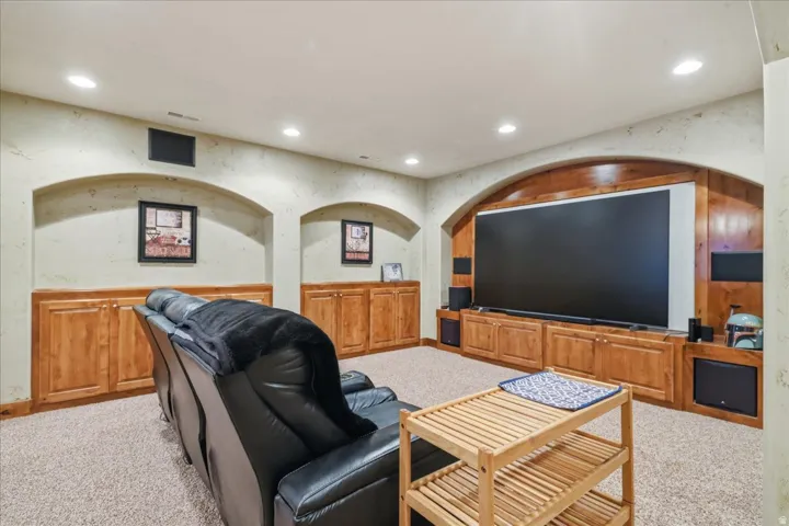 Media room featuring a large screen, integrated sound system, wood-finish cabinetry, recessed ceiling lights, and arched wall details