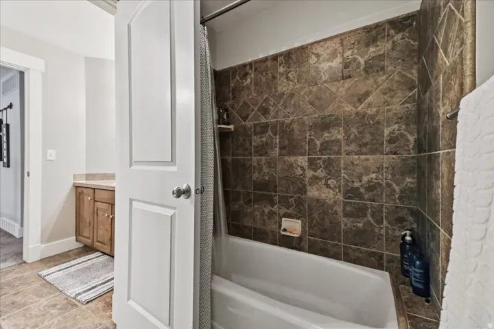 Bathtub with full-height tiled surround, built-in shower shelf, and coordinating tiled flooring
