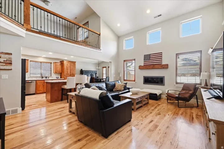 Vaulted ceiling living space with wood-finish flooring, a contemporary linear fireplace, and an upper-level balcony featuring a black spindle railing
