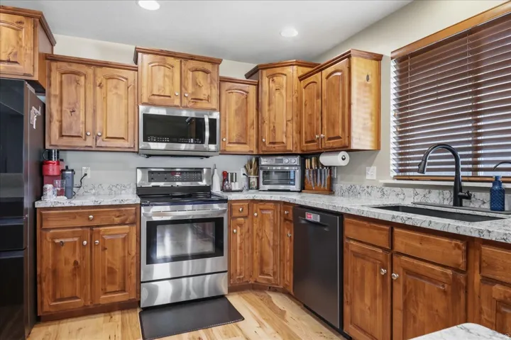 Kitchen featuring wood cabinetry, light-toned countertops, stainless steel appliances, a black sink, and wood-finish flooring