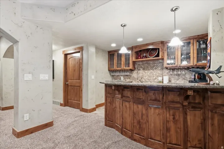 Built-in wet bar with wood cabinetry, stone countertops, and tile backsplash