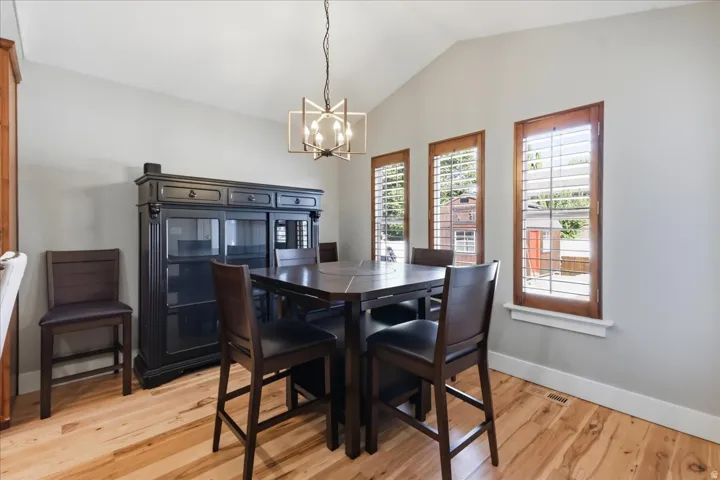 Vaulted ceiling with a contemporary chandelier, wood-finish flooring, and multiple windows with wood plantation shutters