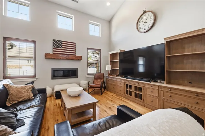 Vaulted ceiling, wood-finish flooring,  modern fireplace with a wood mantel, and multiple windows