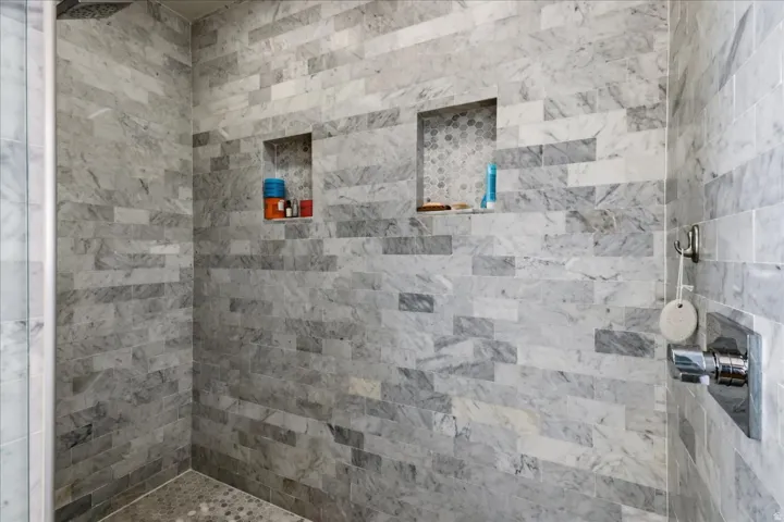 Shower with stacked rectangular tile walls, dual recessed niches featuring mosaic tile accents, and a coordinating mosaic tile floor