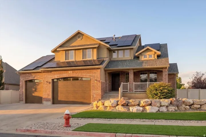 Brick and stucco exterior with multiple gables, solar panels, a covered front porch, and a two-car garage with wood-finish doors