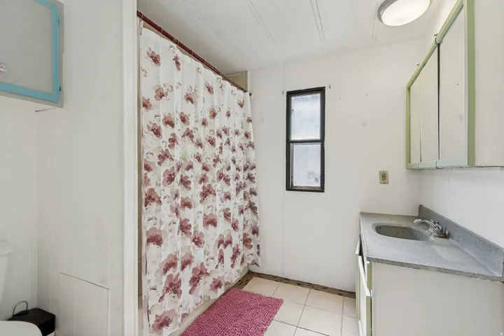 White paneling walls, tile flooring, vanity with integrated sink, wall-mounted mirror cabinet, and an overhead light fixture