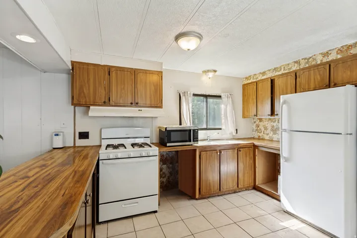 Kitchen featuring wood-finish cabinetry, tile flooring, white gas range, and a white refrigerator