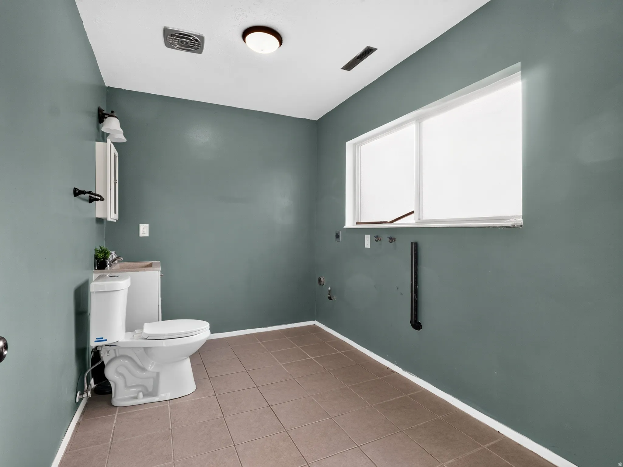 Tile flooring, white toilet, wall-mounted vanity, medicine cabinet, and a large window