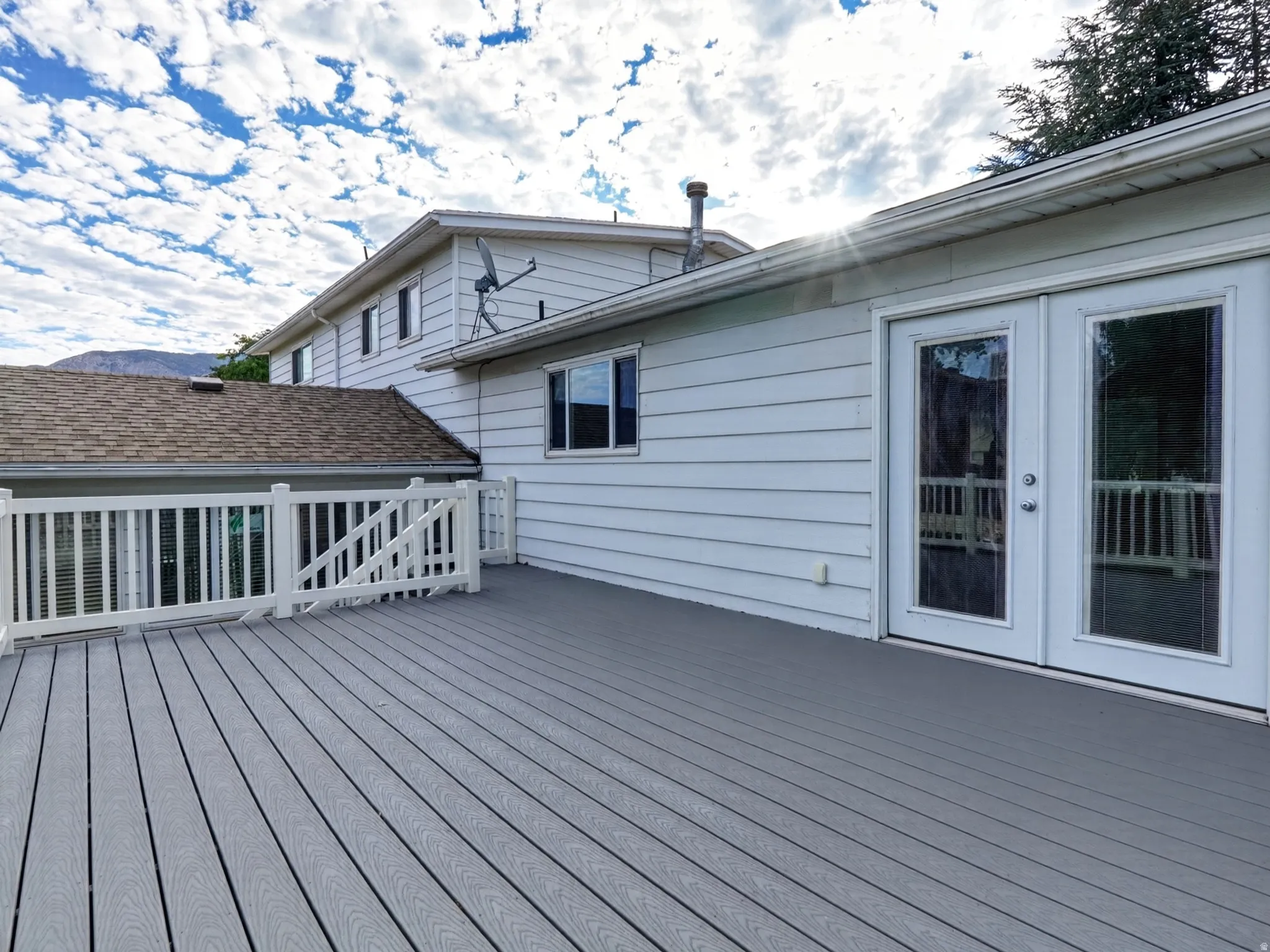 Expansive grey composite decking with white railings and double glass-paneled patio doors