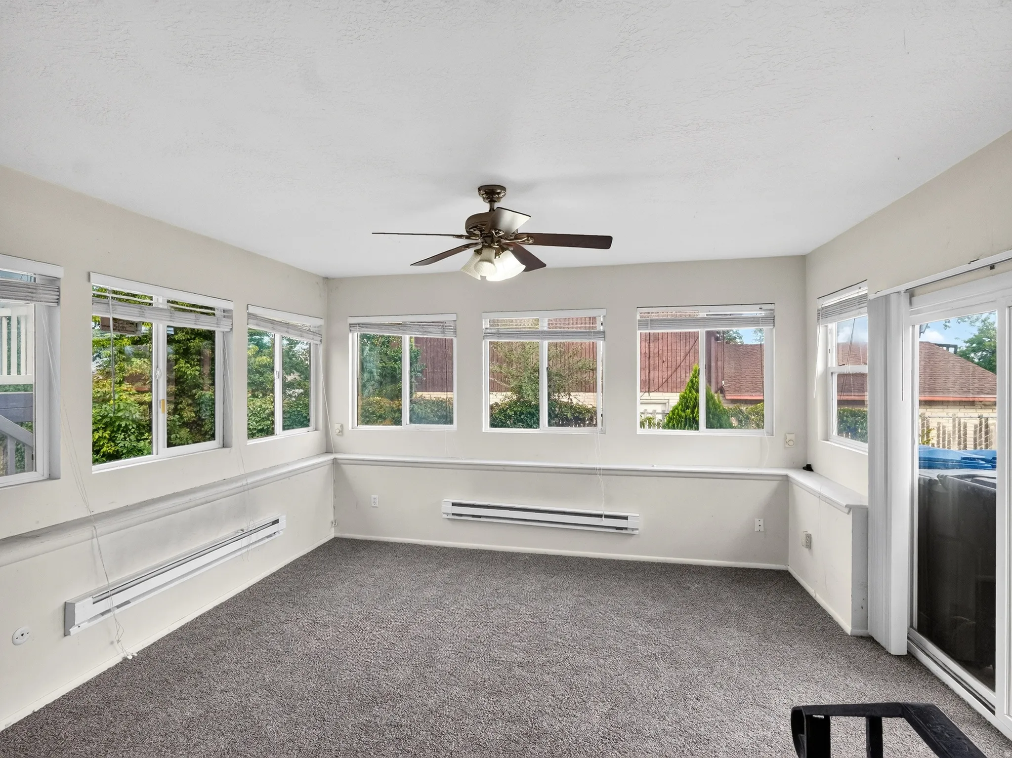 Multiple large windows, gray carpeting, neutral wall finishes, ceiling fan with light fixture, and a sliding glass door