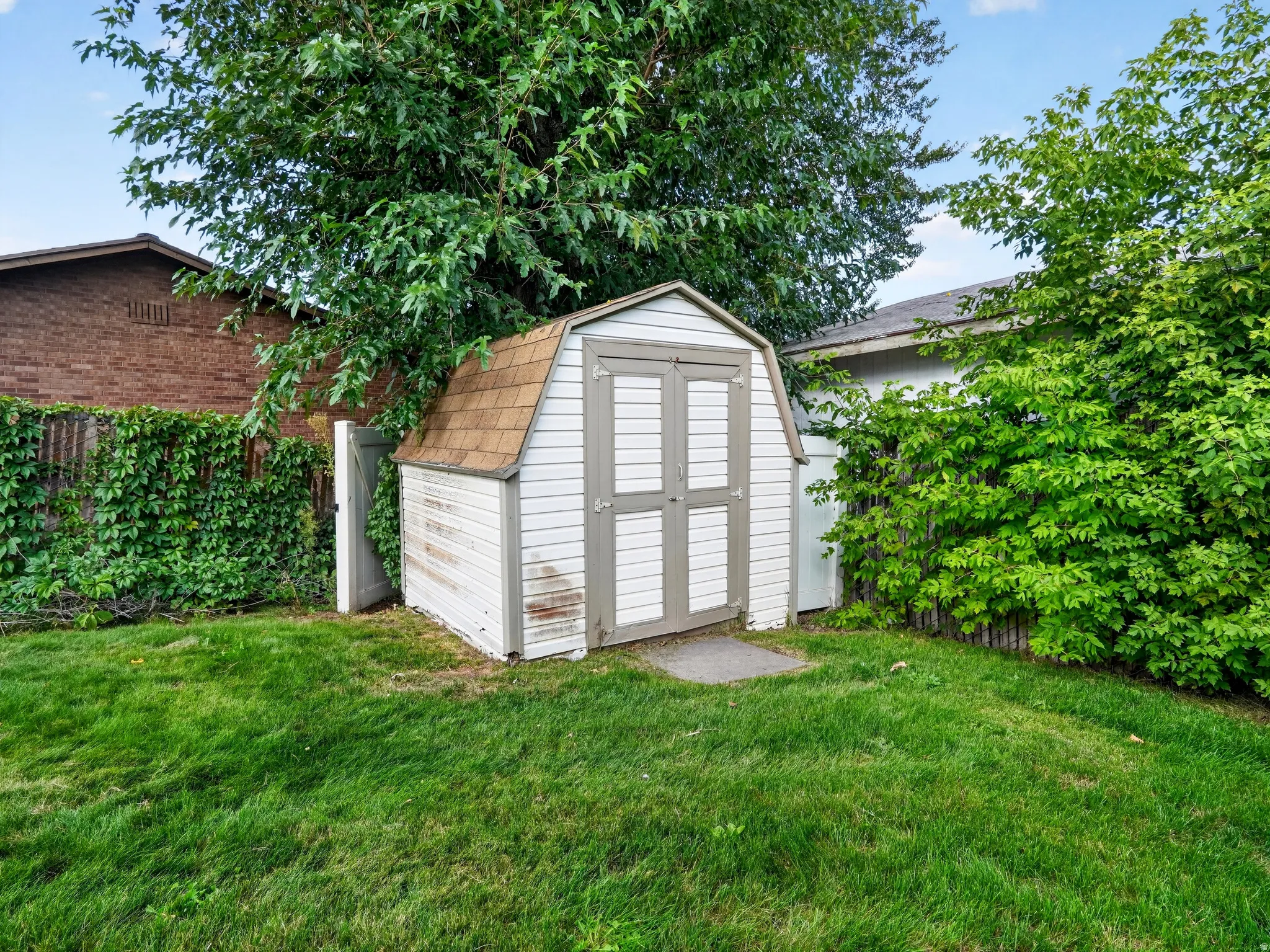 Backyard featuring a storage shed with gambrel roof, a grass lawn, and mature trees