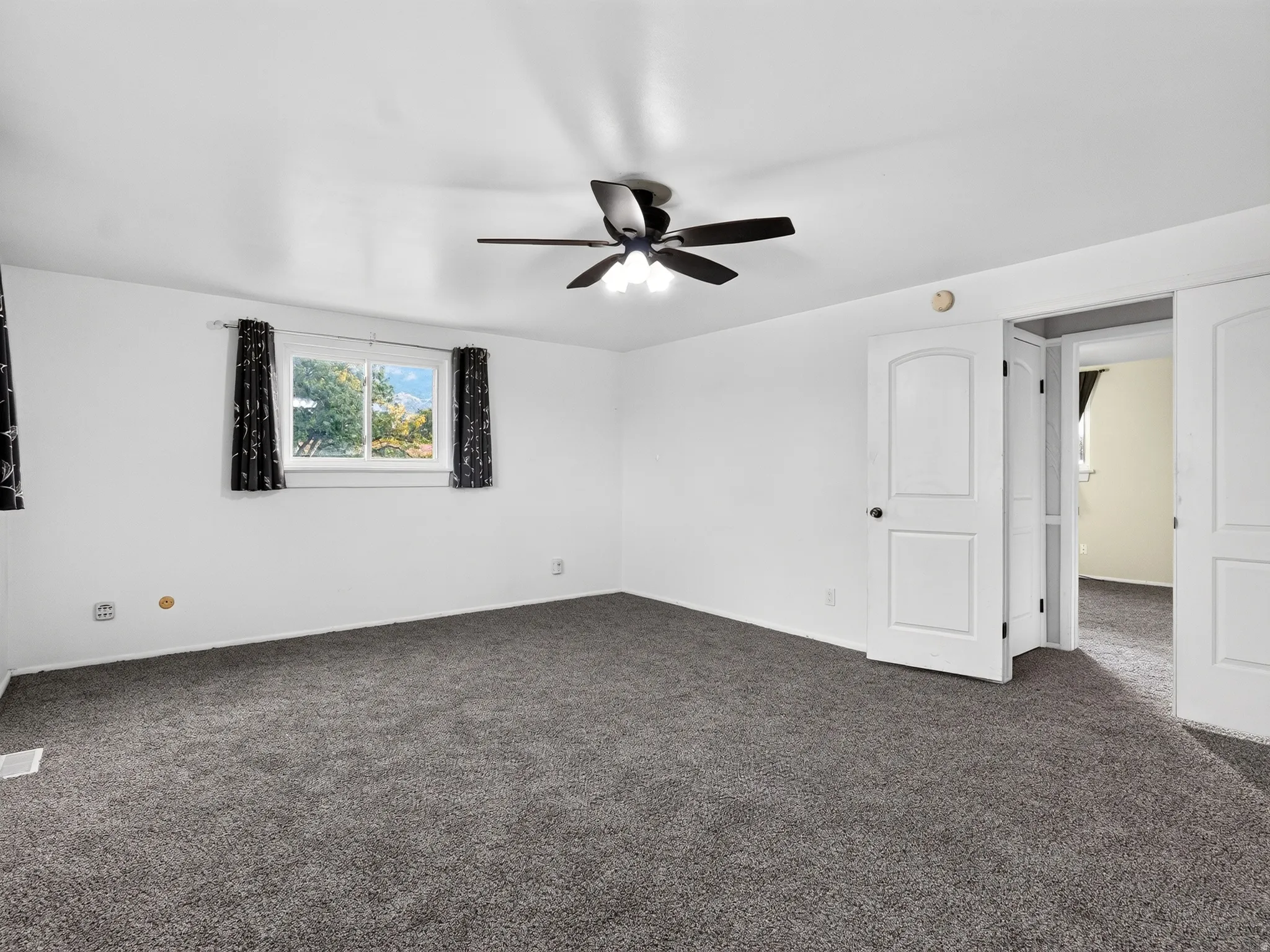 Grey carpet flooring throughout, white walls, two-panel interior doors, and a ceiling fan with integrated lighting