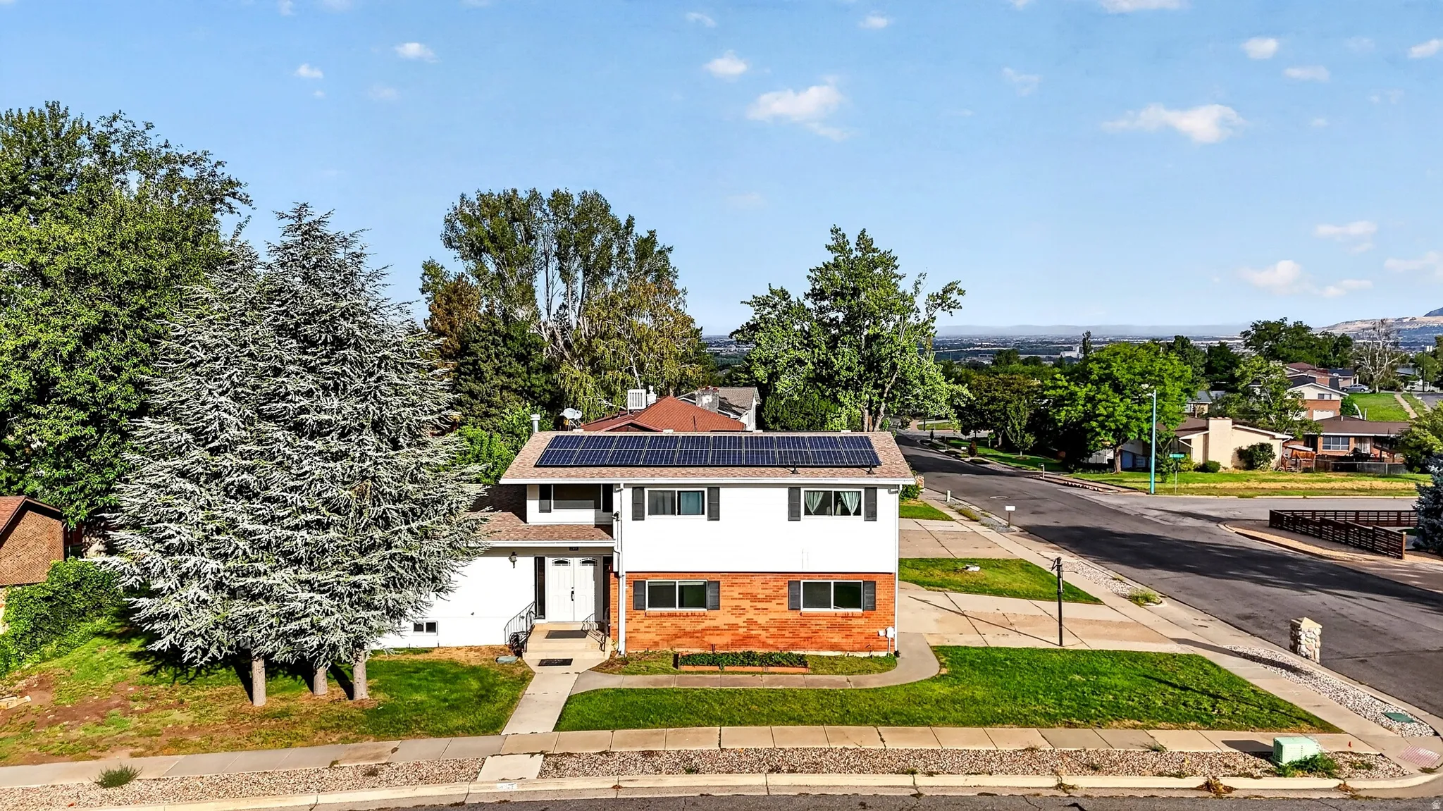 Two-story residence featuring a brick and siding exterior, front yard landscaping, a concrete walkway, and rooftop solar panels