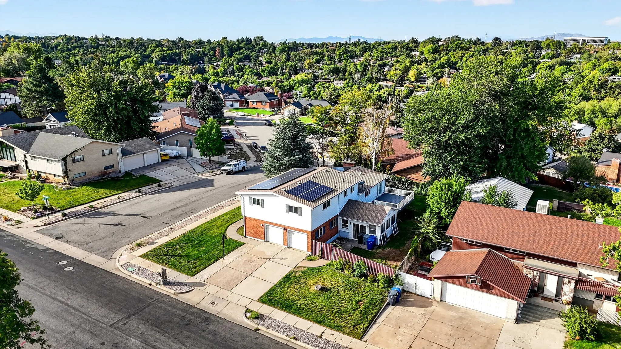 Two-story residence with a brick and siding exterior, integrated solar panels, a two-car garage, and an upper-level deck