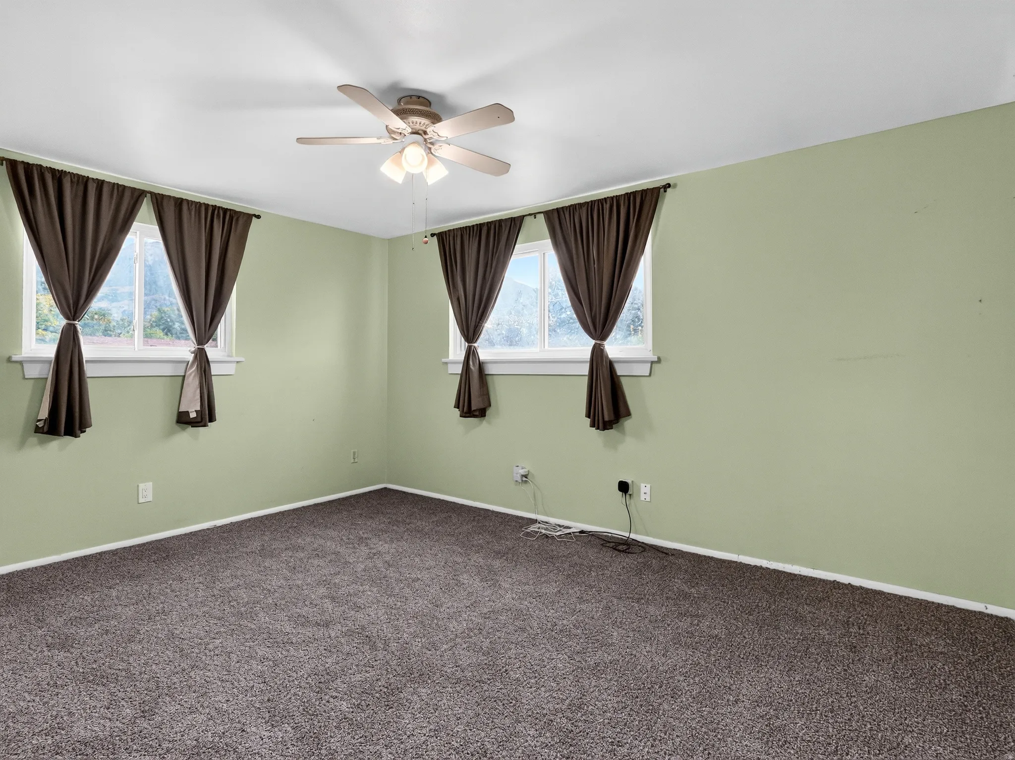 Plush carpet flooring, a ceiling fan with integrated lighting, and multiple windows with curtain rods