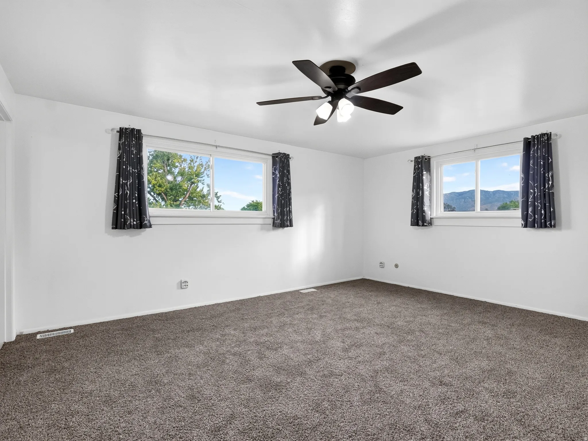 Plush carpeting, bright white walls, two windows, and a ceiling fan with integrated lighting