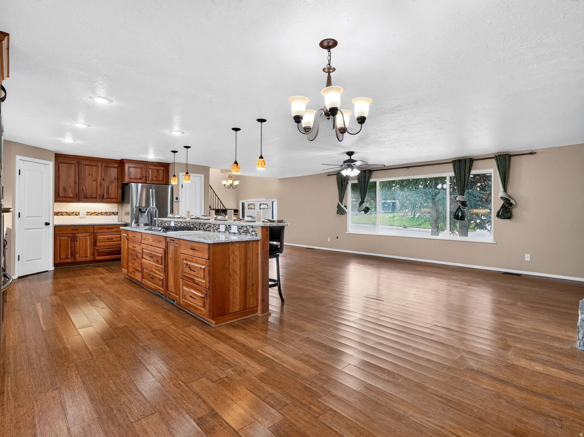 Wood-finish flooring throughout, kitchen island with built-in cabinetry, stainless steel appliances, recessed lighting, and a prominent window