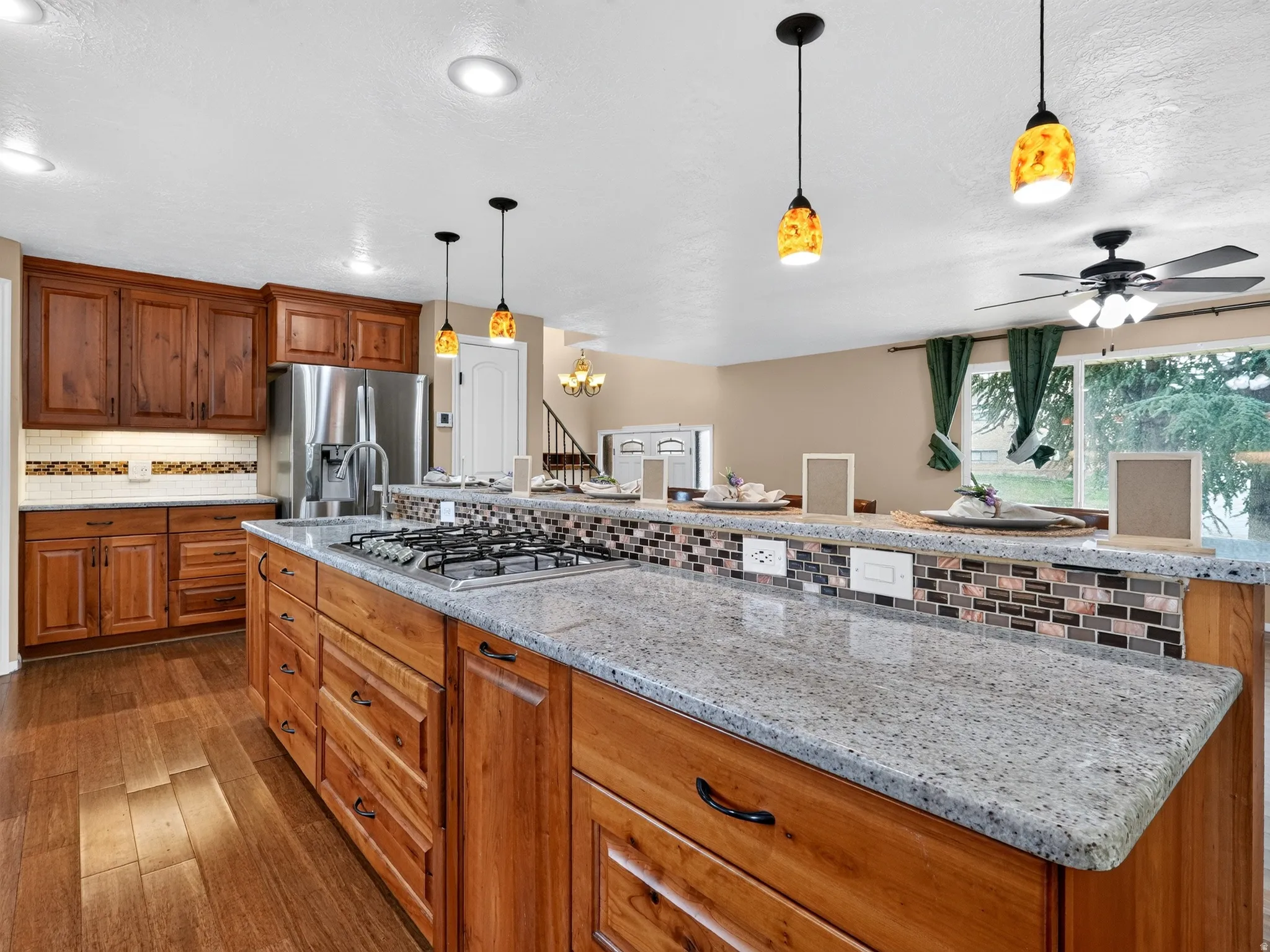 Kitchen featuring wood cabinetry, stainless steel appliances, a center island with a gas cooktop, stone countertops, and wood-finish flooring