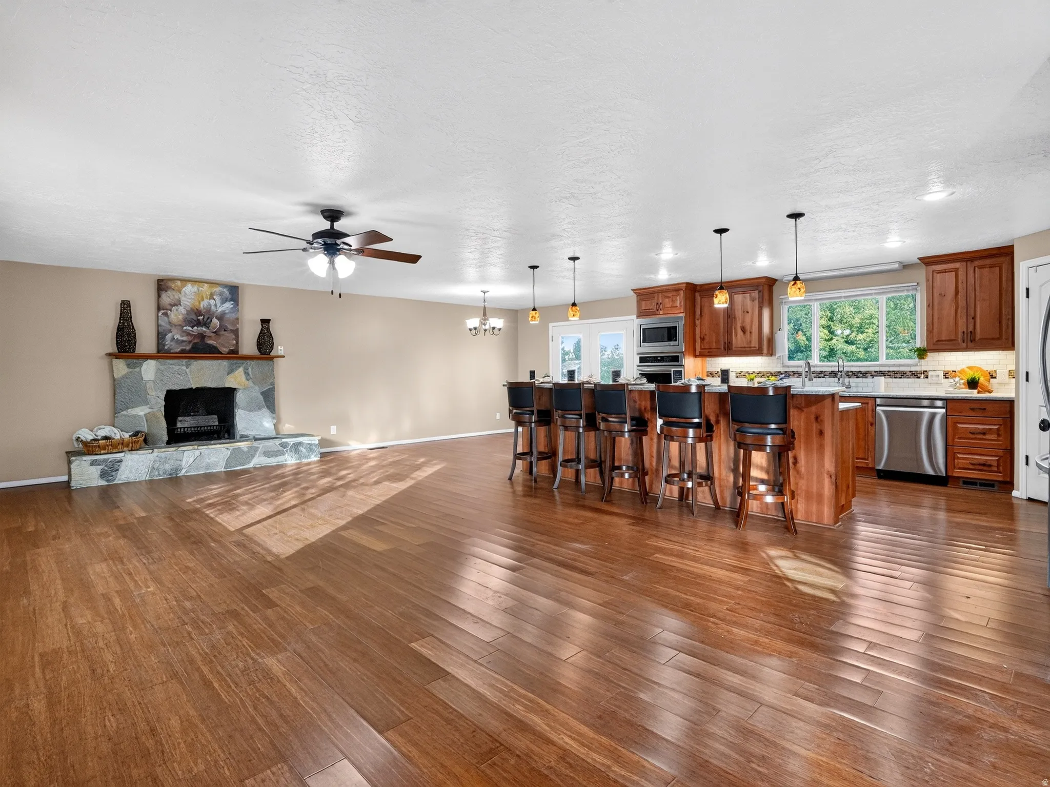 Spacious open-concept interior featuring wood-finish flooring, a stone-clad fireplace, and a kitchen island with pendant lighting