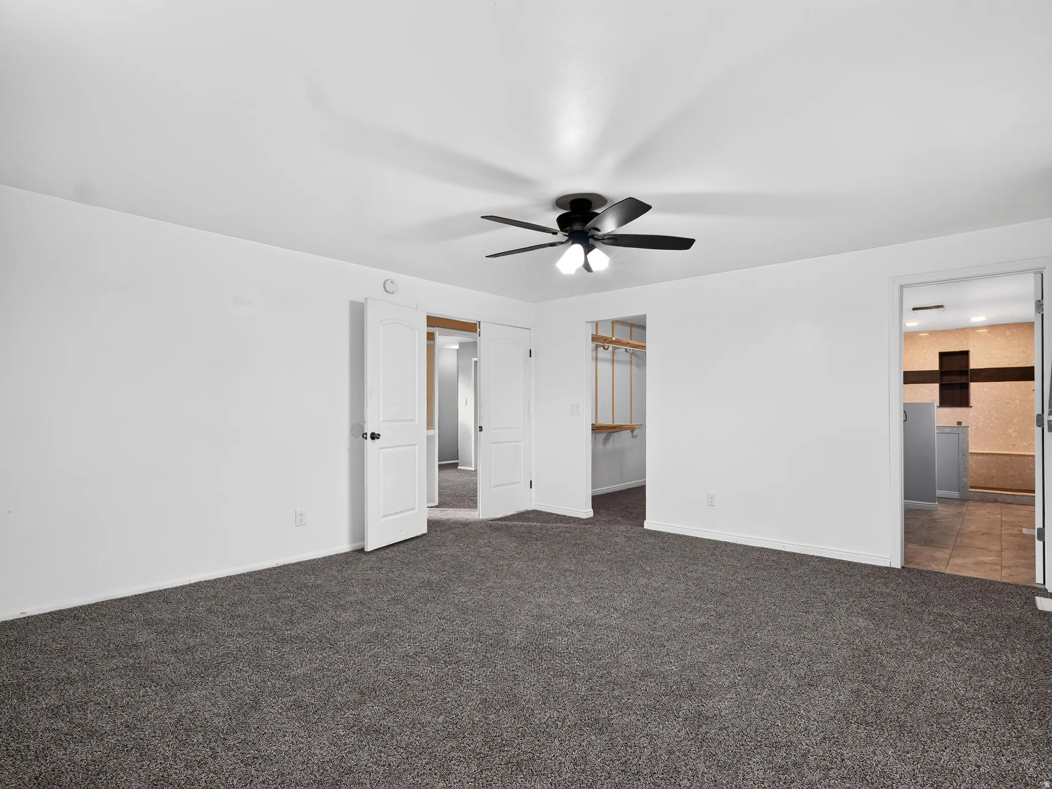 Expansive room featuring dark gray carpeting and a ceiling fan with integrated lighting