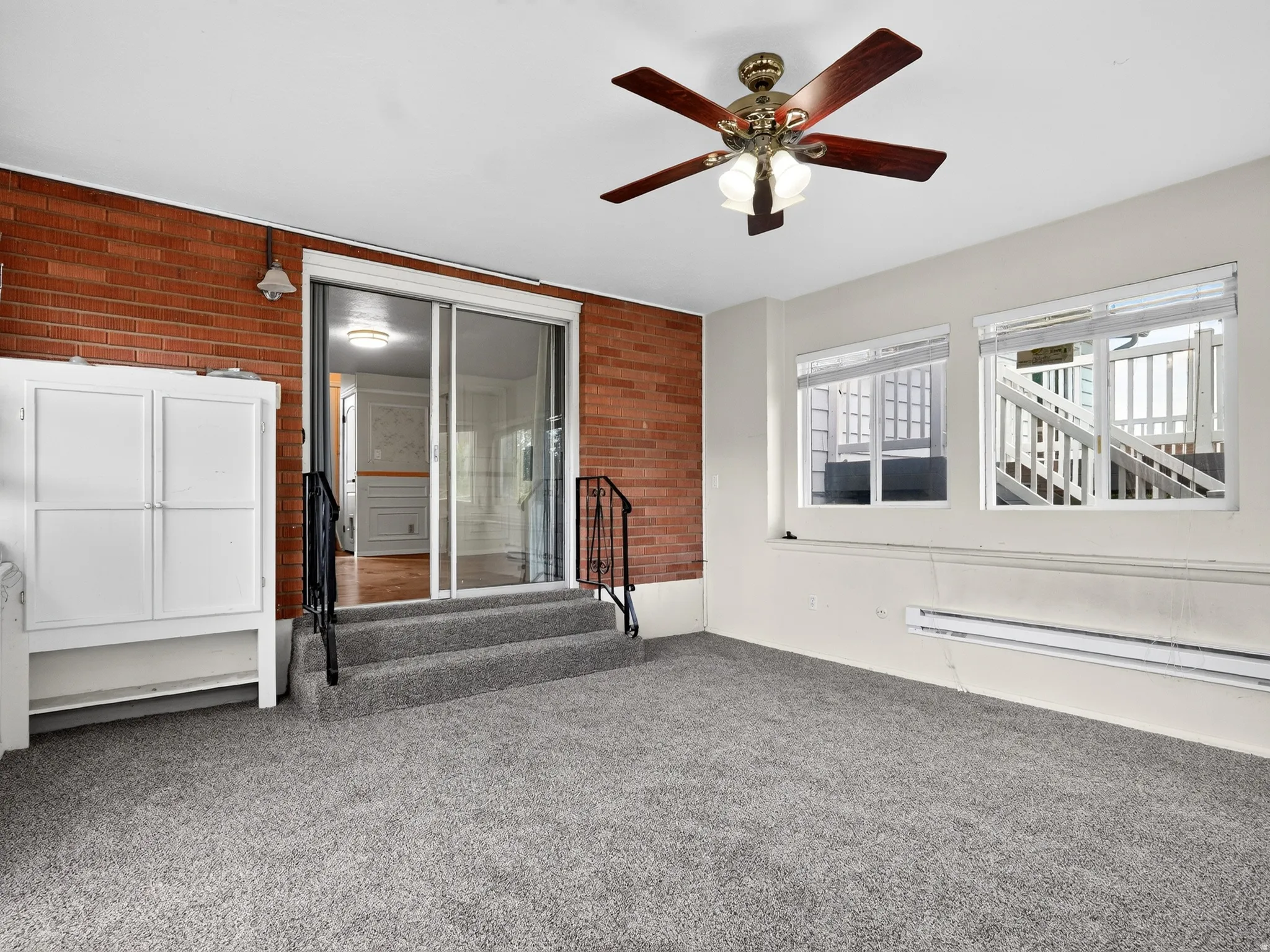 Carpeted room featuring a brick accent wall, ceiling fan, two windows, and a sliding glass door
