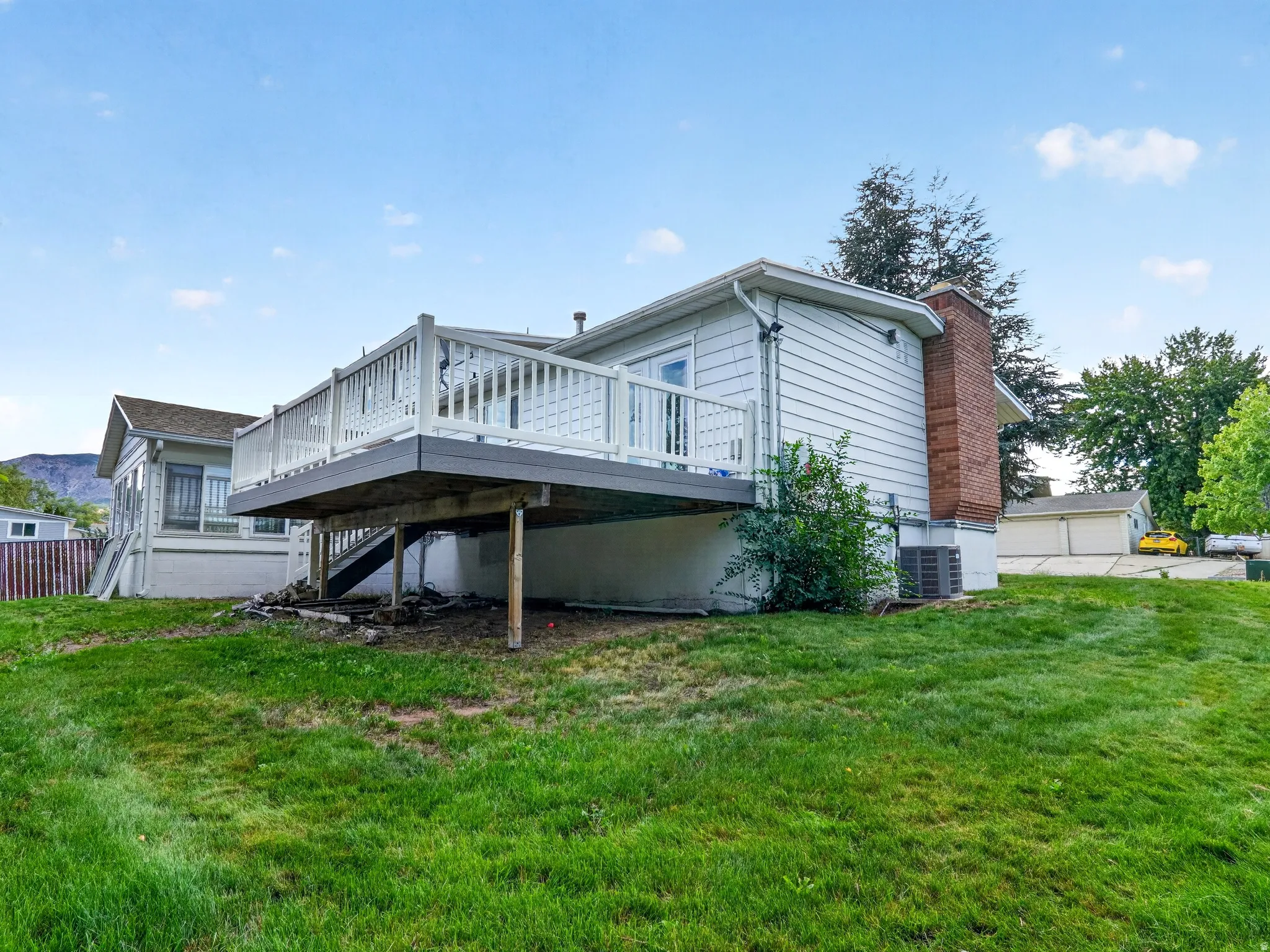 Exterior featuring white siding, a raised deck with white railings, a brick chimney, and a gently sloped lawn