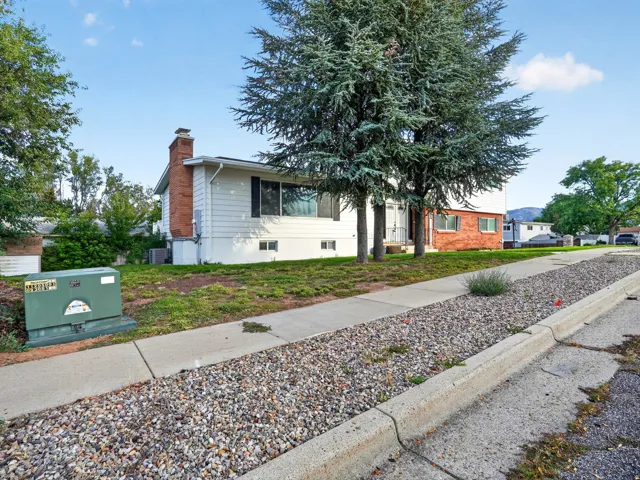 White siding exterior with brick accents, mature trees, and a concrete sidewalk