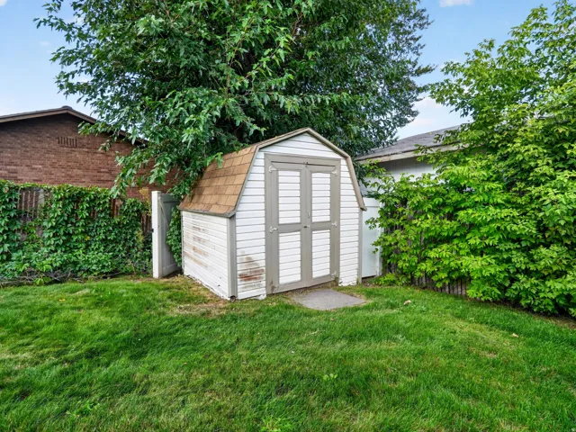 Backyard featuring a storage shed with gambrel roof, a grass lawn, and mature trees