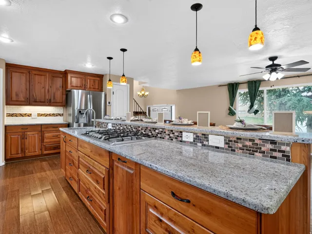 Kitchen featuring wood cabinetry, stainless steel appliances, a center island with a gas cooktop, stone countertops, and wood-finish flooring