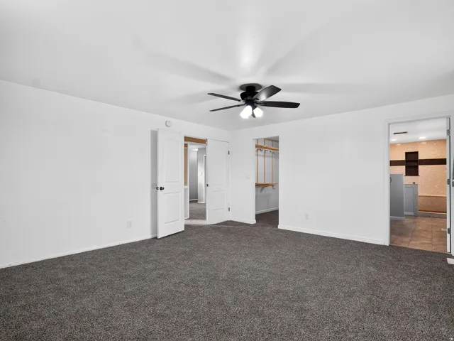 Expansive room featuring dark gray carpeting and a ceiling fan with integrated lighting