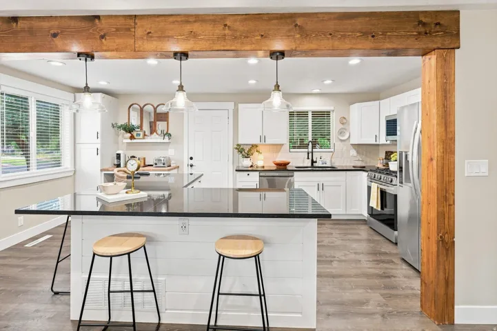 Open-concept kitchen featuring a dark island countertop, white shaker cabinetry, stainless steel appliances, and wood-finish flooring