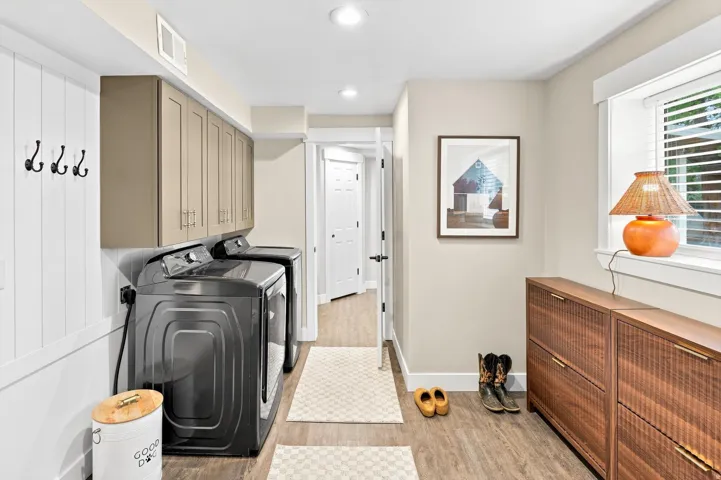 Laundry area featuring a side-by-side washer and dryer, upper cabinetry, wood-finish flooring, and a window with horizontal blinds