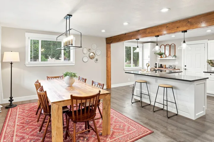 Open-concept dining area with wood-finish flooring, a contemporary linear chandelier, and substantial wood beam accents