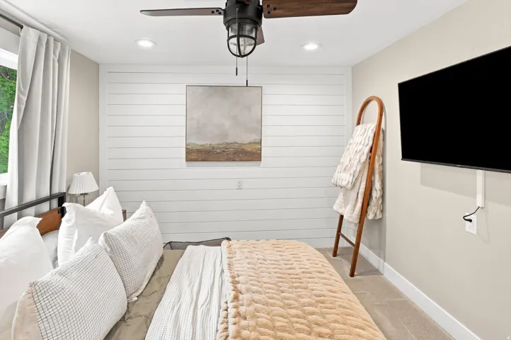 Accent wall with horizontal paneling, recessed lighting, ceiling fan with integrated light, carpet flooring, and a wall-mounted television