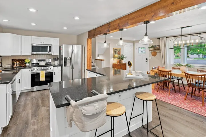 Open-concept kitchen featuring white cabinetry, stainless steel appliances, dark countertops, and wood-finish flooring