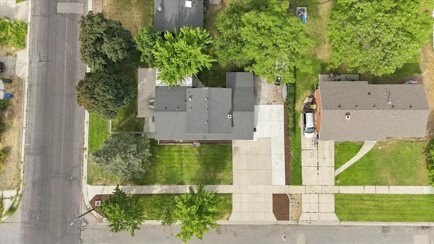 Property featuring a dark shingle roof, concrete driveway, and expansive green lawn