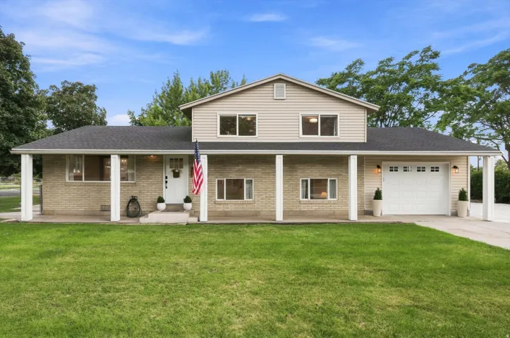 Two-story residence featuring brick and siding exterior, a covered front porch with white columns, attached garage with carriage-style door, and a dark shingle roof
