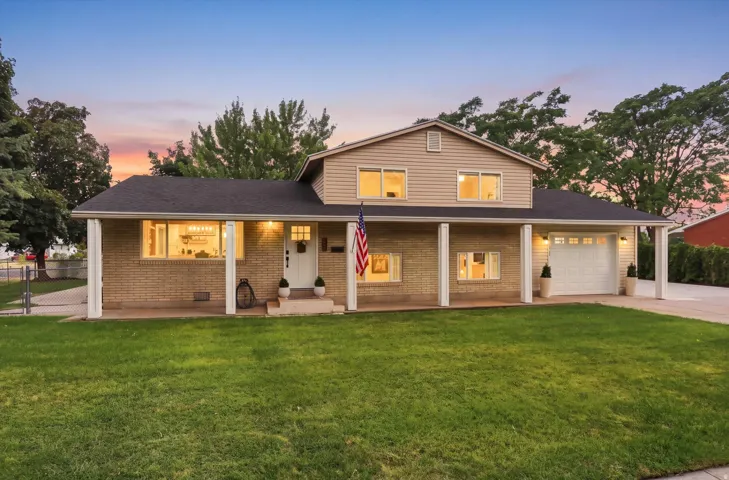 Brick and siding exterior with a covered porch, attached garage, and a manicured lawn