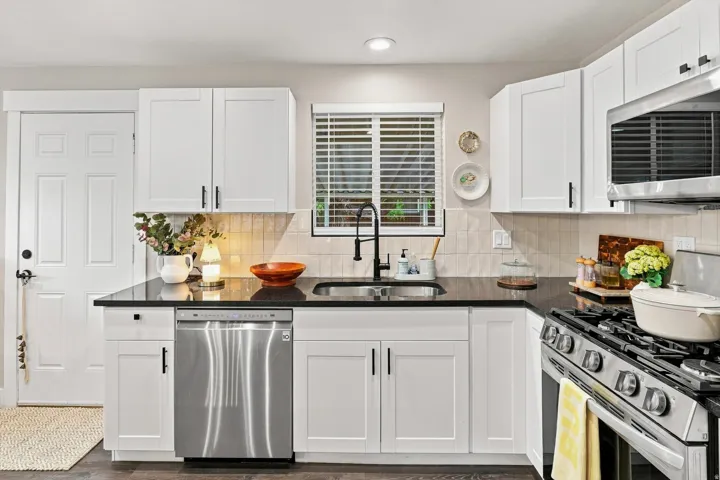 Kitchen featuring white shaker-style cabinetry, dark countertops, a stainless steel dishwasher, a gas range, and wood-finish flooring