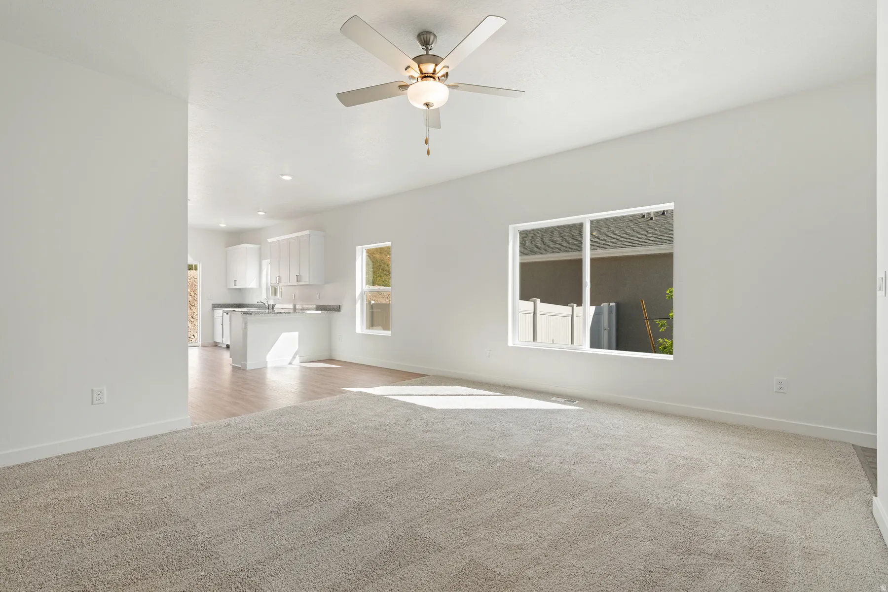 Expansive living area with neutral carpeting, a ceiling fan, and large windows