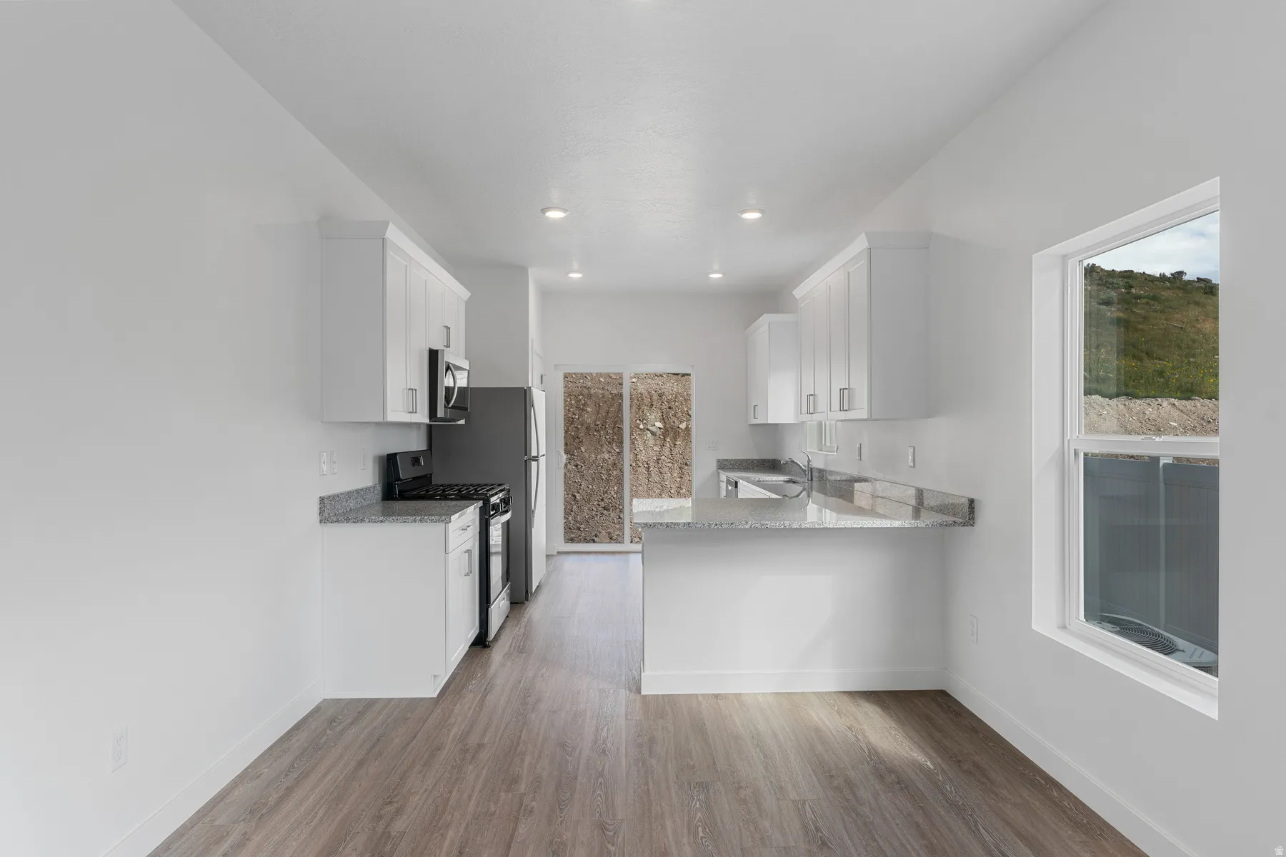 White cabinetry, stainless steel appliances, wood-finish flooring, recessed lighting, and a kitchen island with stone countertops
