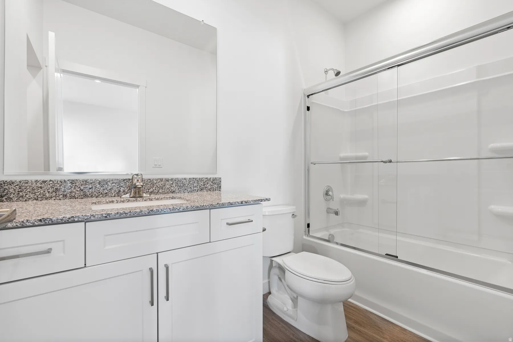 Bathroom featuring a white vanity, stone-finish countertop, single basin sink, and a shower-tub combination with glass enclosure