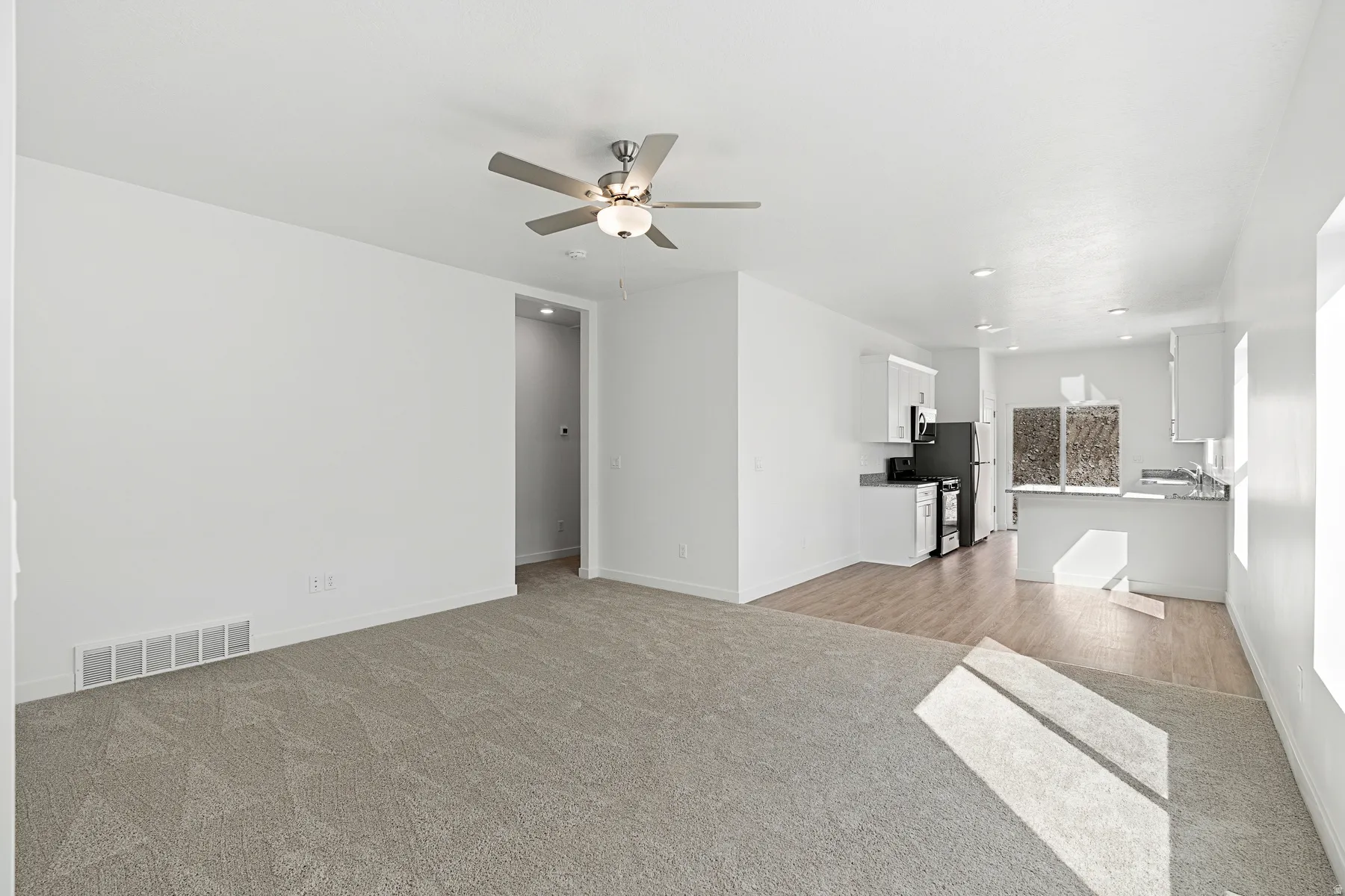 Open-concept living space featuring neutral carpeting, a ceiling fan, and white walls