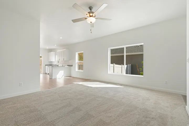 Expansive living area with neutral carpeting, a ceiling fan, and large windows