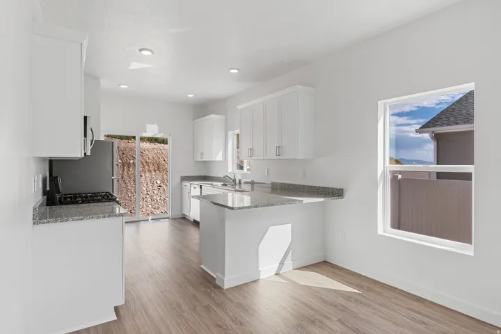 Modern kitchen featuring white cabinetry, granite-finish countertops, wood-finish flooring, recessed lighting, and stainless steel appliances